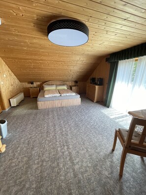 Ein gemütliches Schlafzimmer im Dachgeschoss mit einem großen Bett, Holzwänden, einer Deckenleuchte und Blick ins Freie.