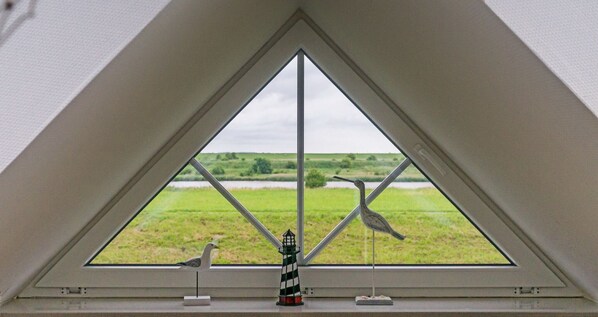 A triangular window with a view of a green landscape and a lighthouse model.