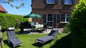 Ein Ziegelhaus mit Terrasse, zwei Liegestühle, einem Tisch mit Stühlen und einem grünen Sonnenschirm.