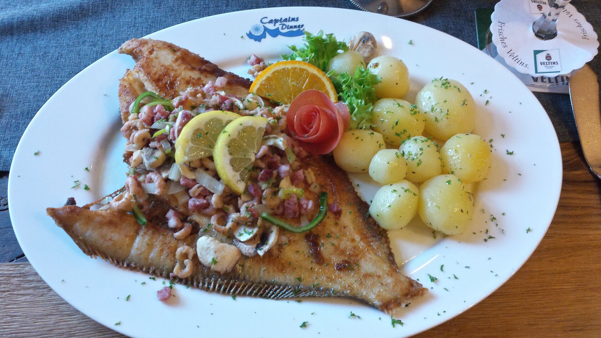 A plate with a fish fillet, lemon slices, a tomato, and boiled potatoes.