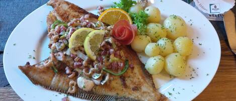 A plate with a fish fillet, lemon slices, a tomato, and boiled potatoes.