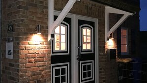 Ein Backsteinhaus mit weiß gefassten Fenstern und einer Tür, beleuchtet durch Außenbeleuchtung.
