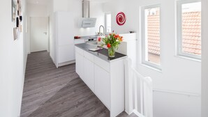 Une cuisine moderne avec des meubles blancs, un îlot central et une vue sur l’extérieur.