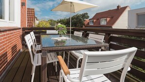 Un espace de restauration en plein air avec une table en verre, des chaises blanches et un parasol beige.