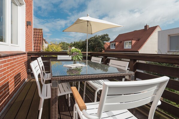 Un espace de restauration en plein air avec une table en verre, des chaises blanches et un parasol beige.