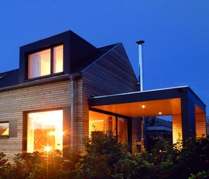 A modern house with a large glass window, a chimney, and a covered outdoor area. - Rent a bungalow, 300 mtr to the beach, private ground, 4 pers. (Ostseeferiendorf Zierow)