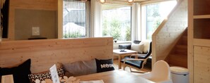 Un interior acogedor de madera con un sofá, una mesa de comedor y una silla. Una ventana ofrece vistas al exterior.