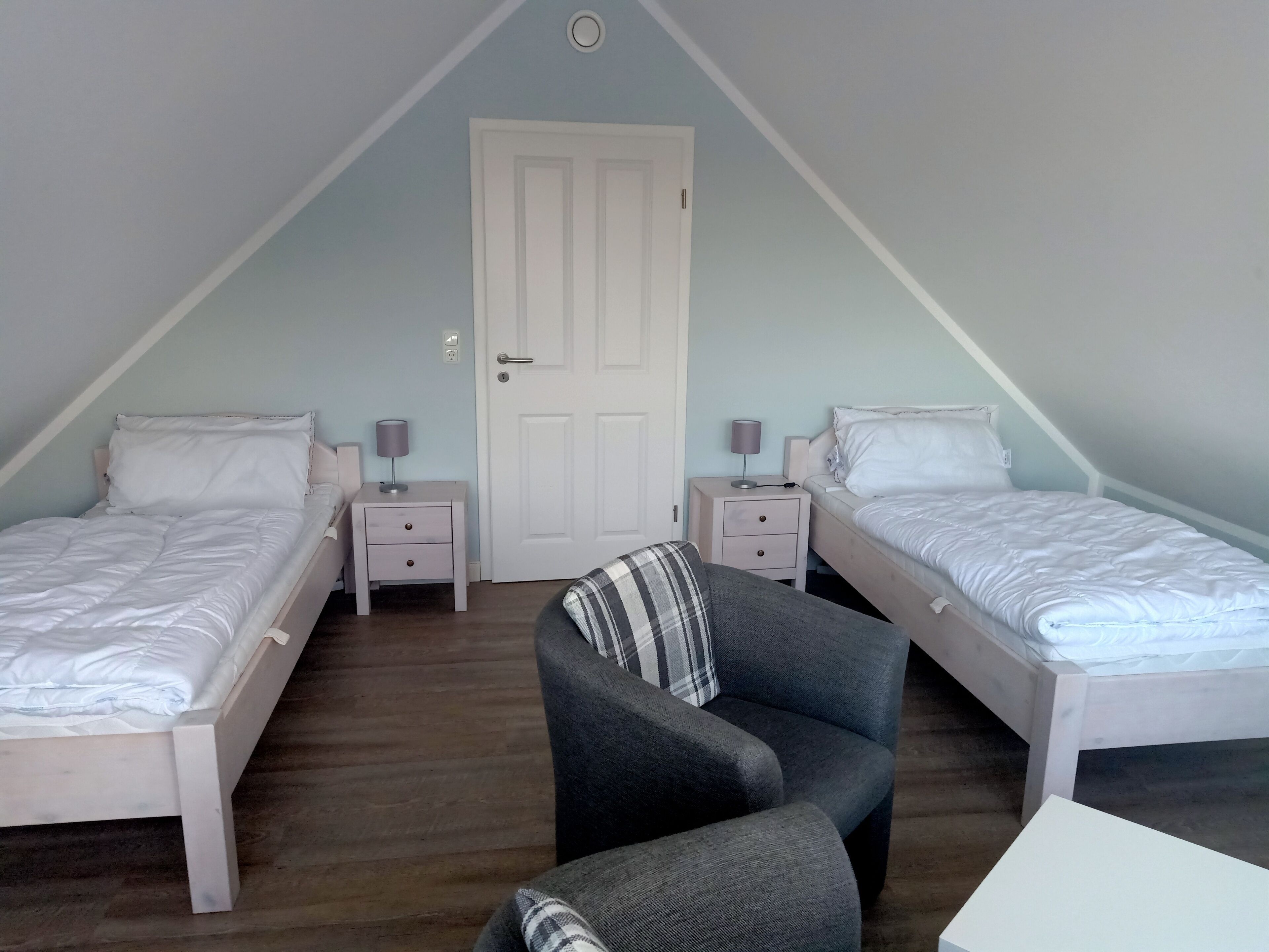 A bedroom with two single beds, a chair, and a desk.