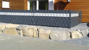 Une maison moderne en bois, dotée d’un mur en pierre et d’une allée pavée.