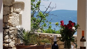 A wooden table set for dining with wine bottles and glasses, a hanging planter with greenery, and a view of the sea and mountains. - Vila Pavincica with swimming pool, soccer pitch and award-winning honey tasting (LABIN)