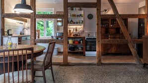 Uma cozinha rústica com vigas de madeira, uma mesa de jantar com cadeiras e diversos eletrodomésticos e utensílios de cozinha.