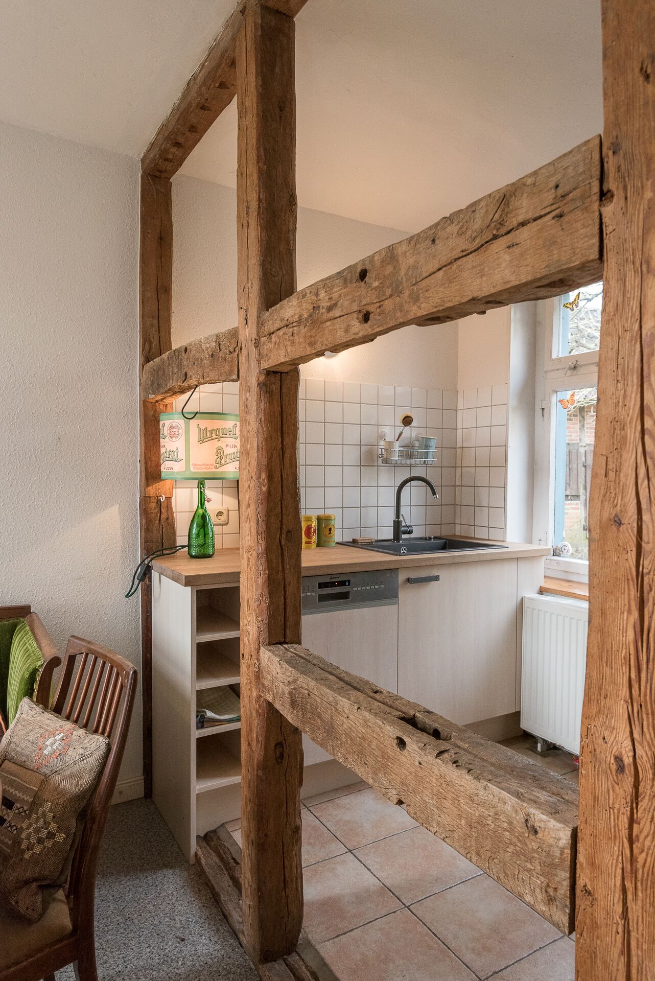 Una cocina con vigas de madera, salpicadero de azulejos, lavavajillas y ventana con vistas.