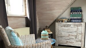 A cozy room with a wicker chair, a small round table, and a rustic chest of drawers.