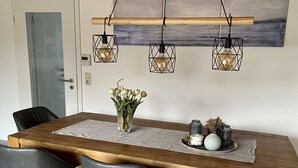 A dining area with a wooden table, four black chairs, a vase of flowers, and three hanging light fixtures.