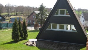 Een huis in een driehoekige vorm, met twee zichtbare ramen en een klein terras.