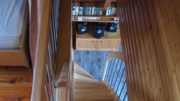 Een houten trap die naar een lager gelegen niveau leidt, met een boekenkast en een koffieapparaat op de overloop.