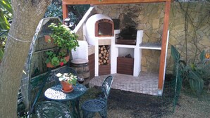 A stone-built outdoor kitchen with a brick oven, surrounded by a wire fence, and featuring a table and chairs. - Apartment m. Pool u. Sea view, about 500m to the beach in Sesimbra for max. 4 pers (Sesimbra)