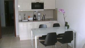 A compact kitchen with white cabinets, a microwave, a coffee maker, and a sink. There is a dining table with four chairs. - Apartment m. Pool u. Sea view, about 500m to the beach in Sesimbra for max. 4 pers (Sesimbra)
