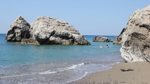 Ein Strand mit großen Felsformationen und klarem, blauem Wasser.
