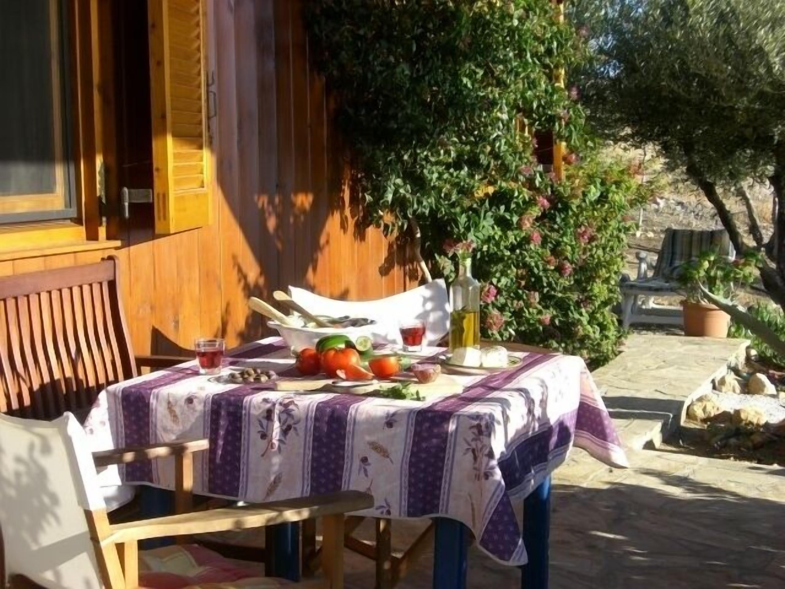 A wooden table with a purple tablecloth, a bowl of fruit, and a bottle of olive oil.