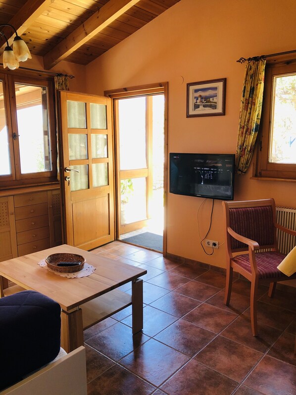 A cozy room with a wooden table, a chair, a television, and a door leading outside.