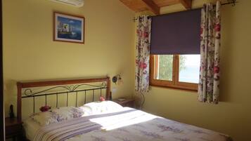A bedroom with a bed, a window with curtains, a wall-mounted air conditioner, and a framed picture.