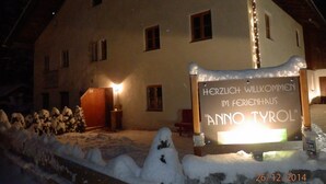 Lumipeitteinen rakennus, jonka yläpuolella on kyltti, jossa lukee: ”Lämpimästi tervetuloa lomamökkiin Anno Tyrol.”