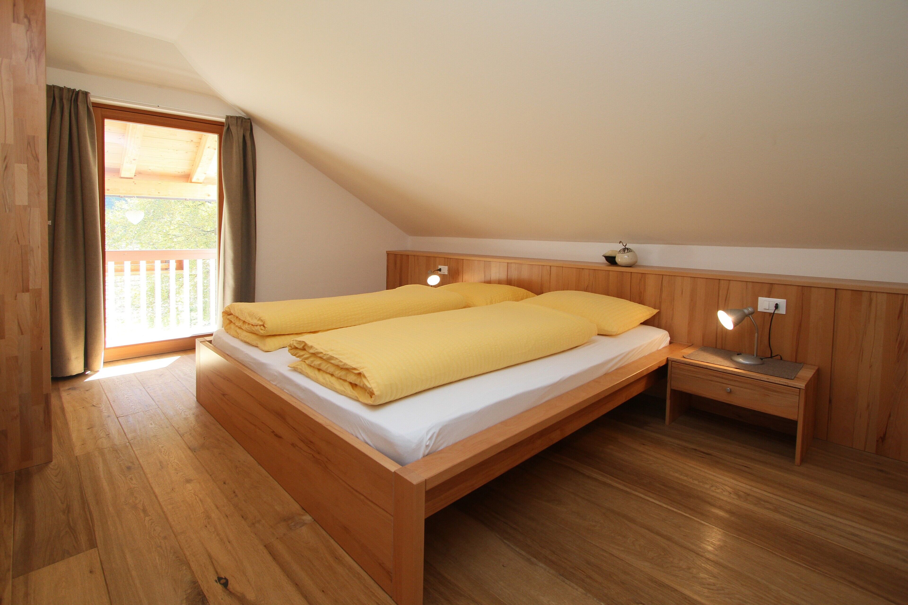 A bedroom with a wooden bed, a nightstand, a lamp, and a window with curtains.