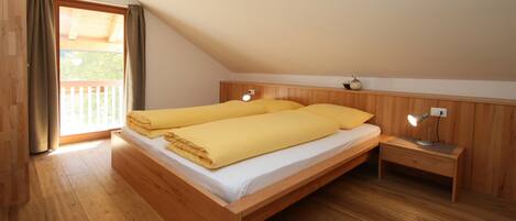 A bedroom with a wooden bed, a nightstand, a lamp, and a window with curtains.