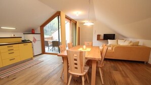A dining area with a wooden table and chairs, a yellow kitchen with a refrigerator, and a sofa in a corner. - New and fully furnished apartment! Calm and relaxation guaranteed! (St. Lorenzen)