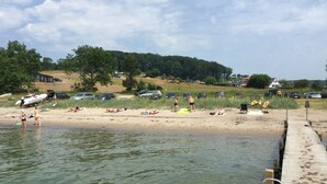 A beach with clear water, a wooden dock, and parked cars.