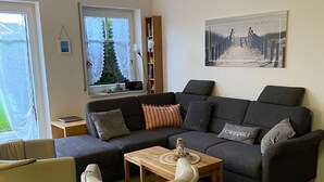 Een woonkamer met een bank, fauteuils, een salontafel, een boekenkast en een schilderij aan de muur.