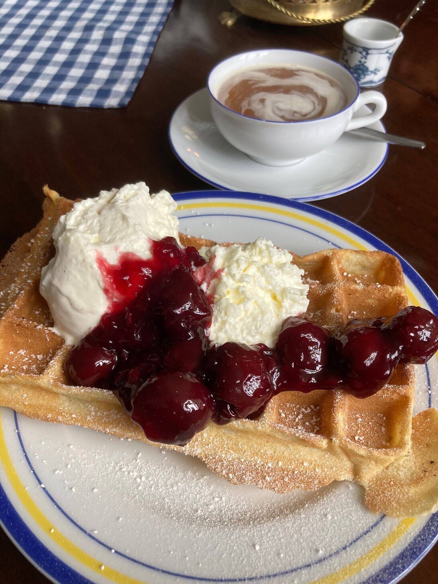 A plate of waffles with whipped cream and cherries, a cup of coffee, and a small cup of tea on a table.