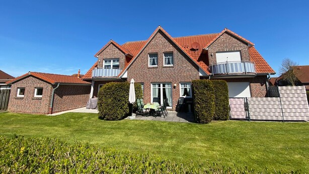 Een tweelaags bakstenen huis met een rode dakbedekking, een voortuin en een verzorgd gazon.