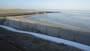 Een strand met een verharde looppad en een lage betonnen muur.