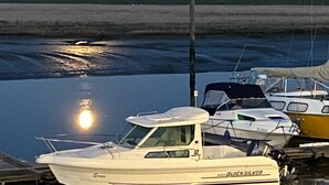 Een jachthaven met aangemeerde boten, een rustig wateroppervlak dat de maan weerspiegelt, en een heldere lucht.