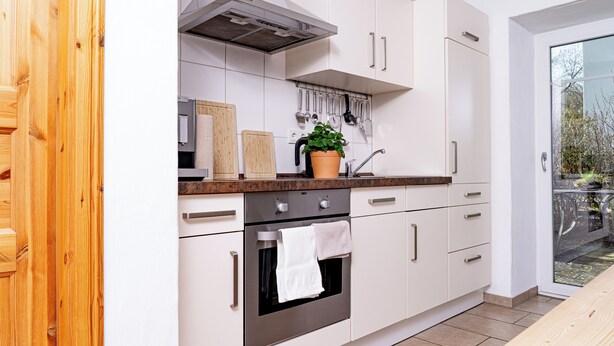 A modern kitchen with white cabinetry, a stainless steel oven, a wooden countertop, and a potted plant.