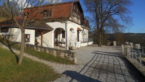 A traditional building with a sloped roof, stone walls, and a gravel driveway leading to a wooden fence.