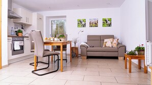 A modern living room with a sofa, a dining table with chairs, a kitchen area, and artwork on the wall.