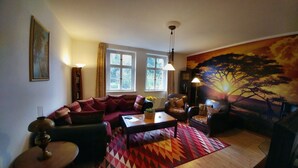Een woonkamer met een bank, fauteuils, een salontafel en een groot schilderij van een boom.