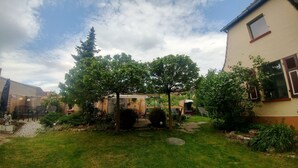 Een tuin met een houten pergola, een pad van stenen en een klein zitgedeelte met stoelen.