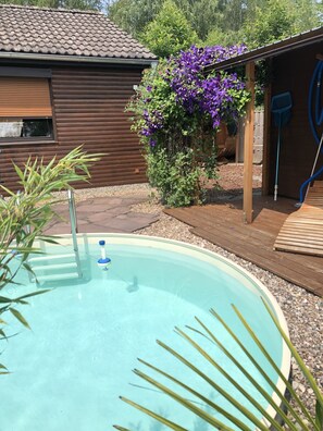 En swimmingpool med træterrasse, omgivet af en træhytte og frodig vegetation.