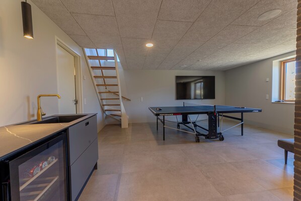 A room with a ping pong table, a sink, a staircase, and a TV mounted on the wall. - Modern vacation home: sea view, 4 bedrooms, 2 bathrooms, beach 100 m, terrace (Grenaa)