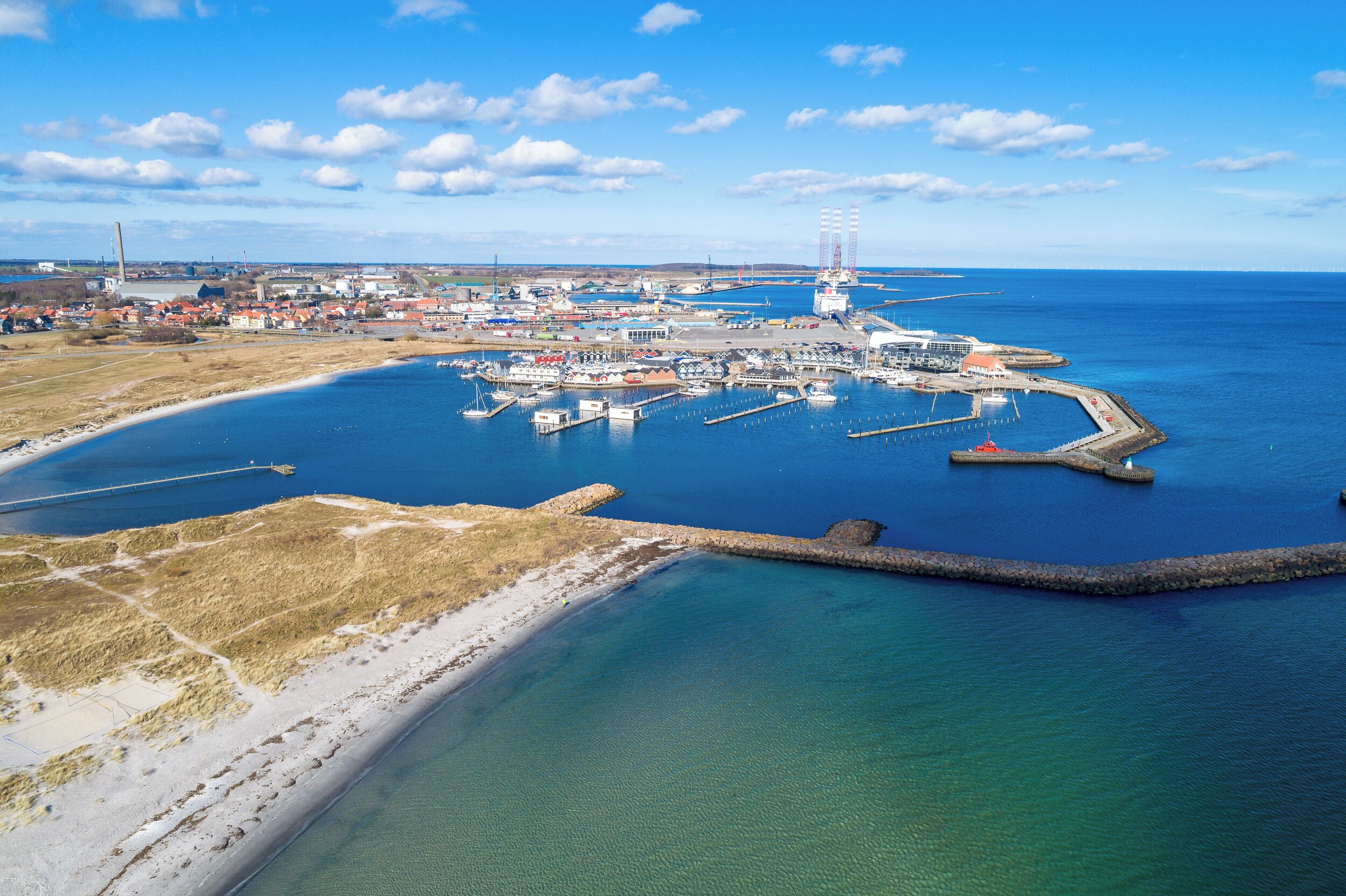 An aerial view of a coastal marina with docks, boats, and a lighthouse.