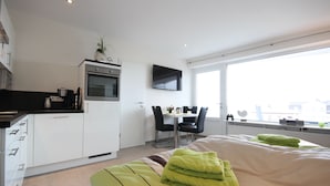 Une chambre d’hôtel moderne équipée d’un lit, d’une petite kitchenette, d’un coin repas et d’une grande fenêtre.