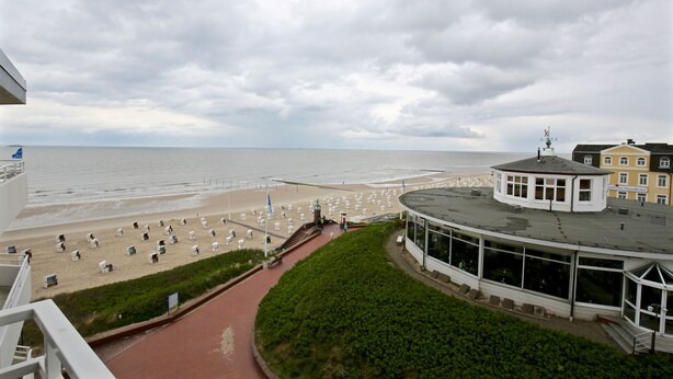 Une vue sur la plage avec une promenade menant à la mer, un kiosque et un bâtiment doté de grandes fenêtres.