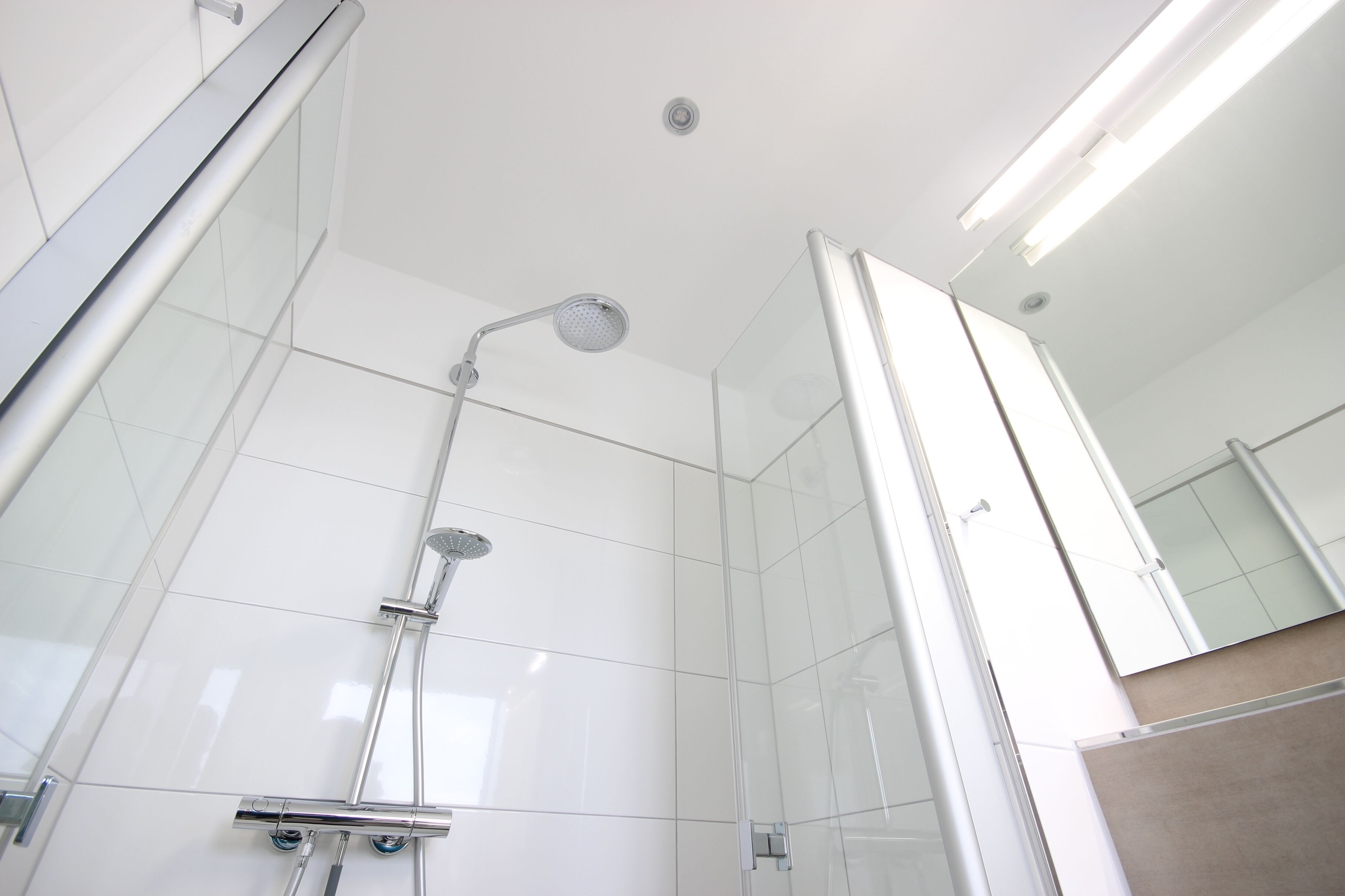 Een moderne douche met een glazen douchecabine, een handdouche en een wandmengkraan.