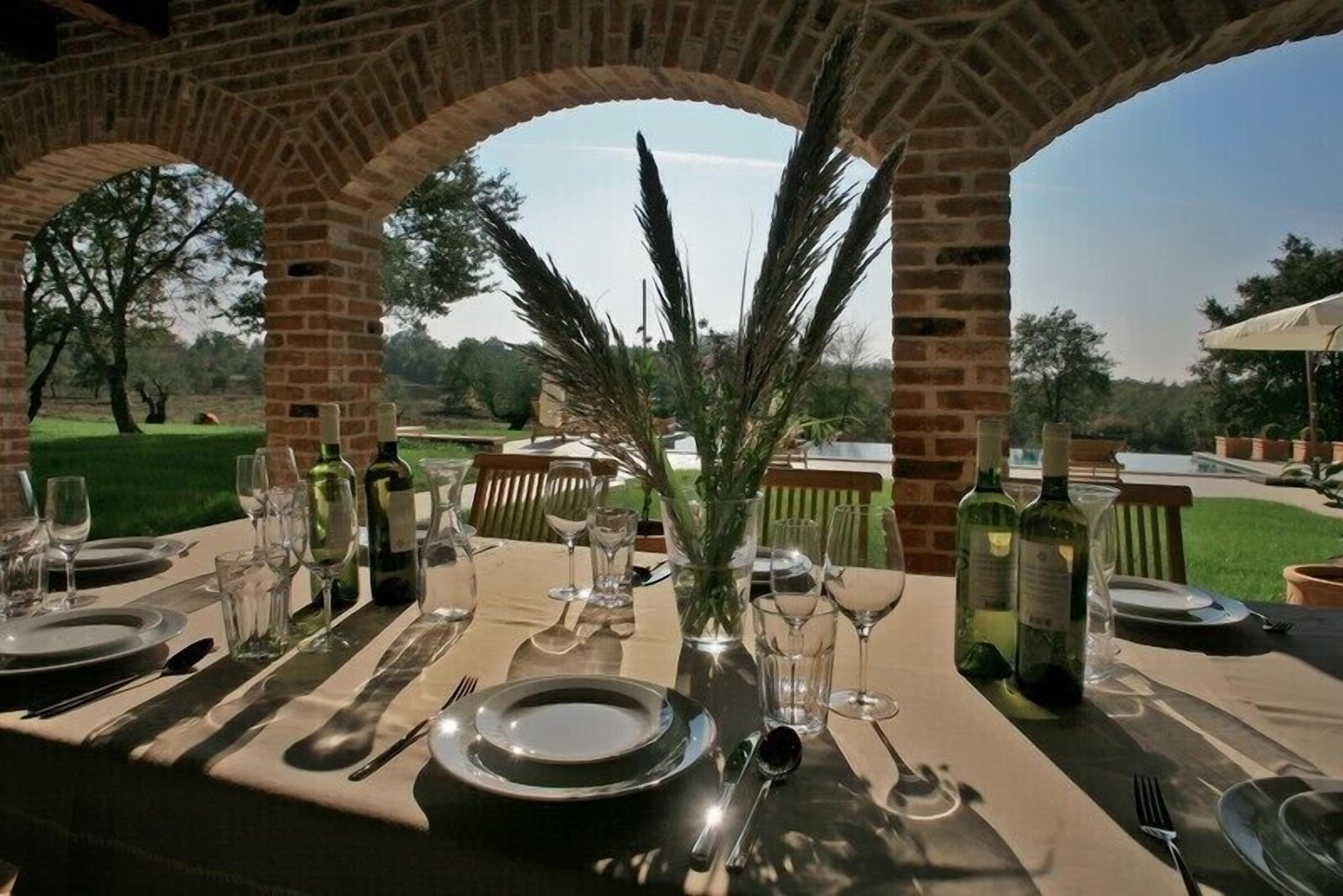 An outdoor dining area with a brick archway, a table set for a meal, and a view of the surrounding landscape.