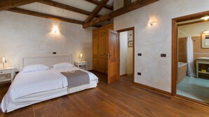 Un dormitorio con techo de madera, una cama grande, un armario de madera y un baño visible a través de una puerta abierta.