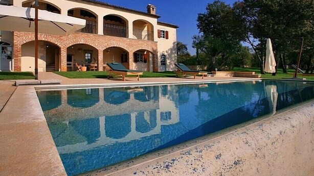 Una casa grande con piscina, mobiliario de exterior y un patio cubierto.